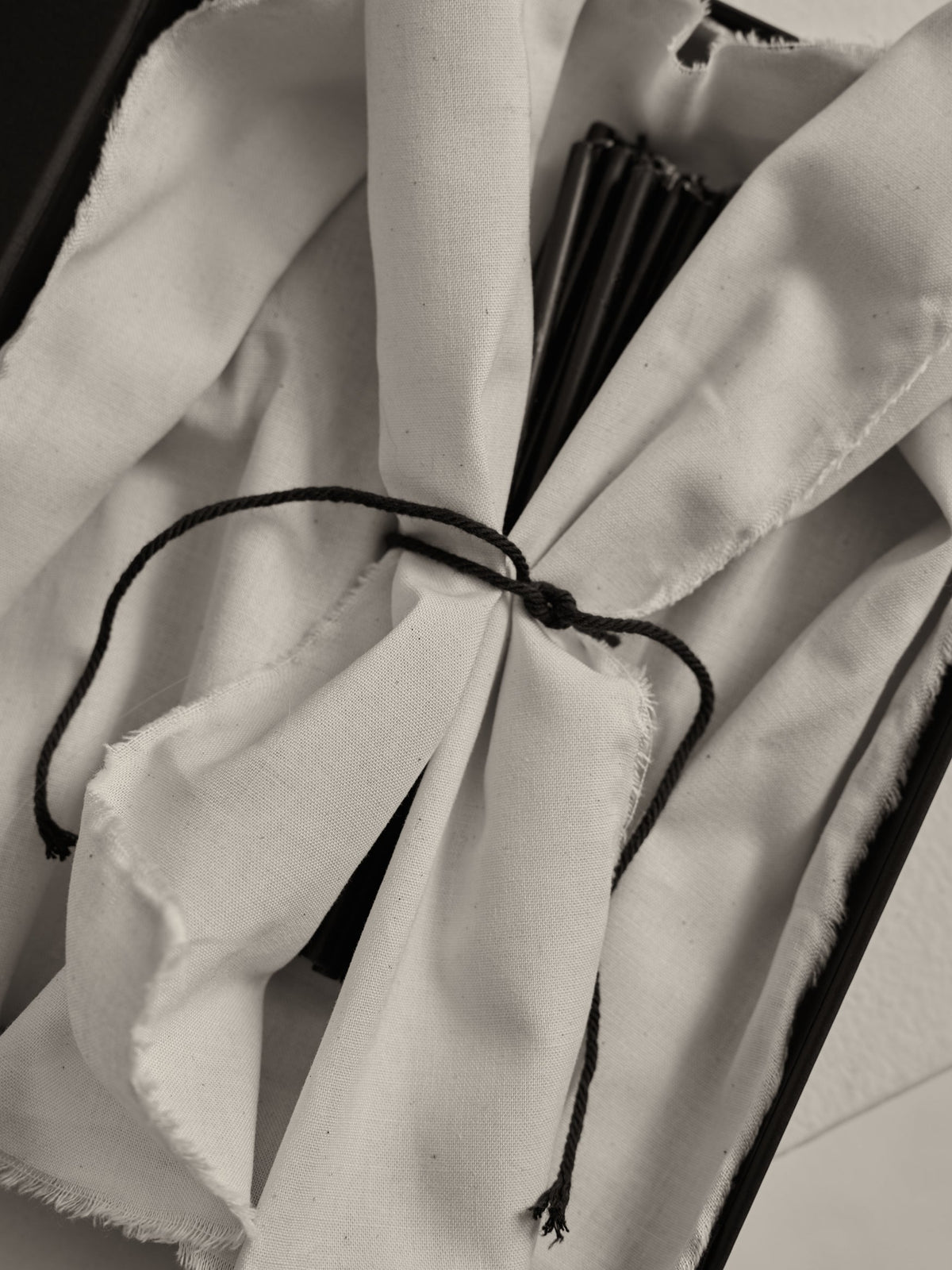 Close-up of Candles 10mm | noir, wrapped in white cloth, tied with black cord, partially revealing black rib-like slats, suggesting a folded hand-fan.
