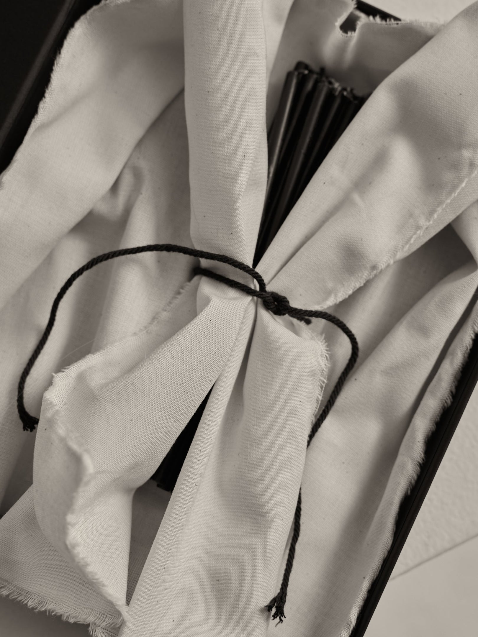 Close-up of Candles 10mm | noir, wrapped in white cloth, tied with black cord, partially revealing black rib-like slats, suggesting a folded hand-fan.