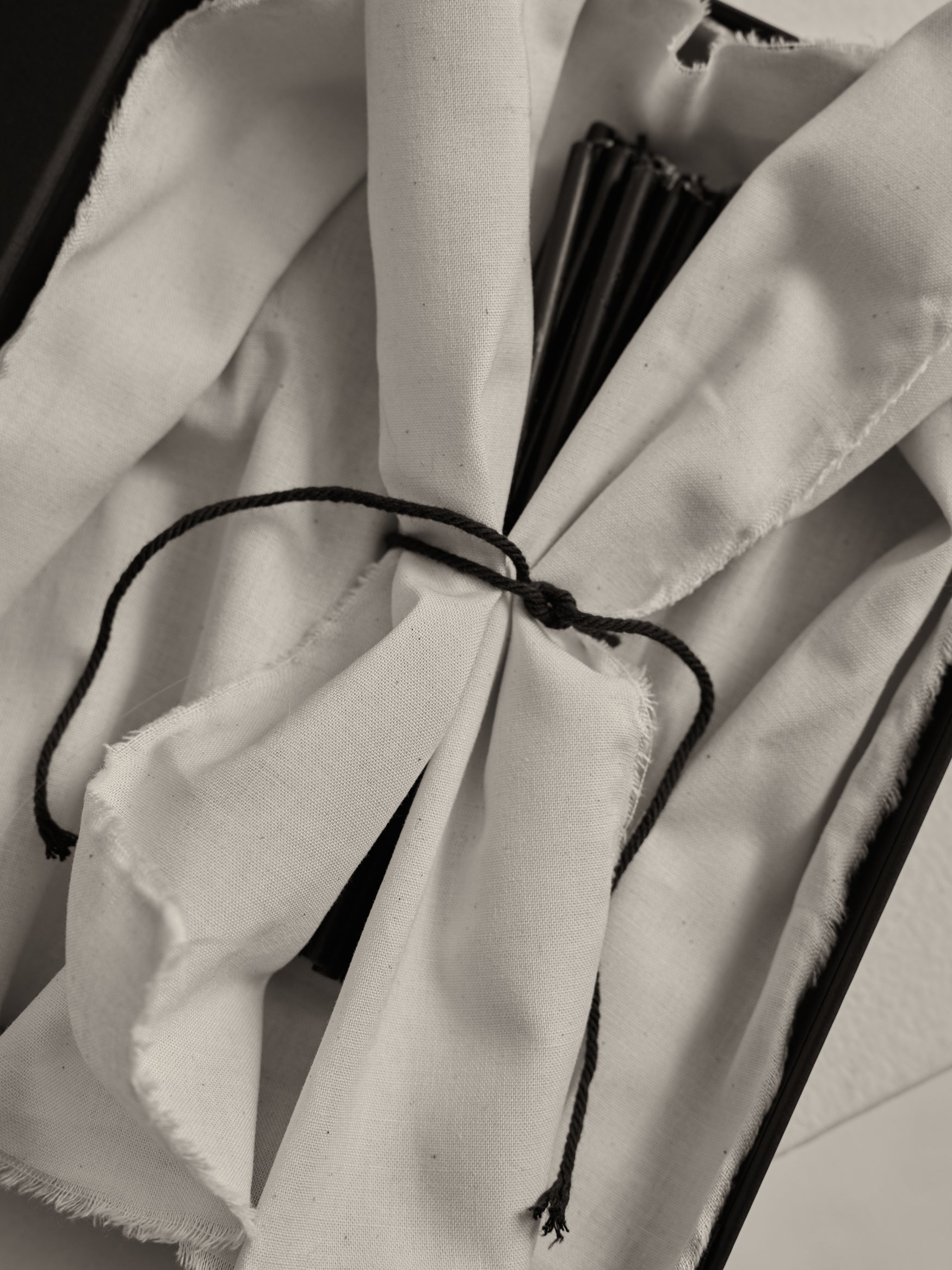Close-up of Candles 10mm | noir, wrapped in white cloth, tied with black cord, partially revealing black rib-like slats, suggesting a folded hand-fan.