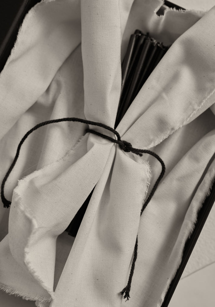 Close-up of Candles 10mm | noir, wrapped in white cloth, tied with black cord, partially revealing black rib-like slats, suggesting a folded hand-fan.