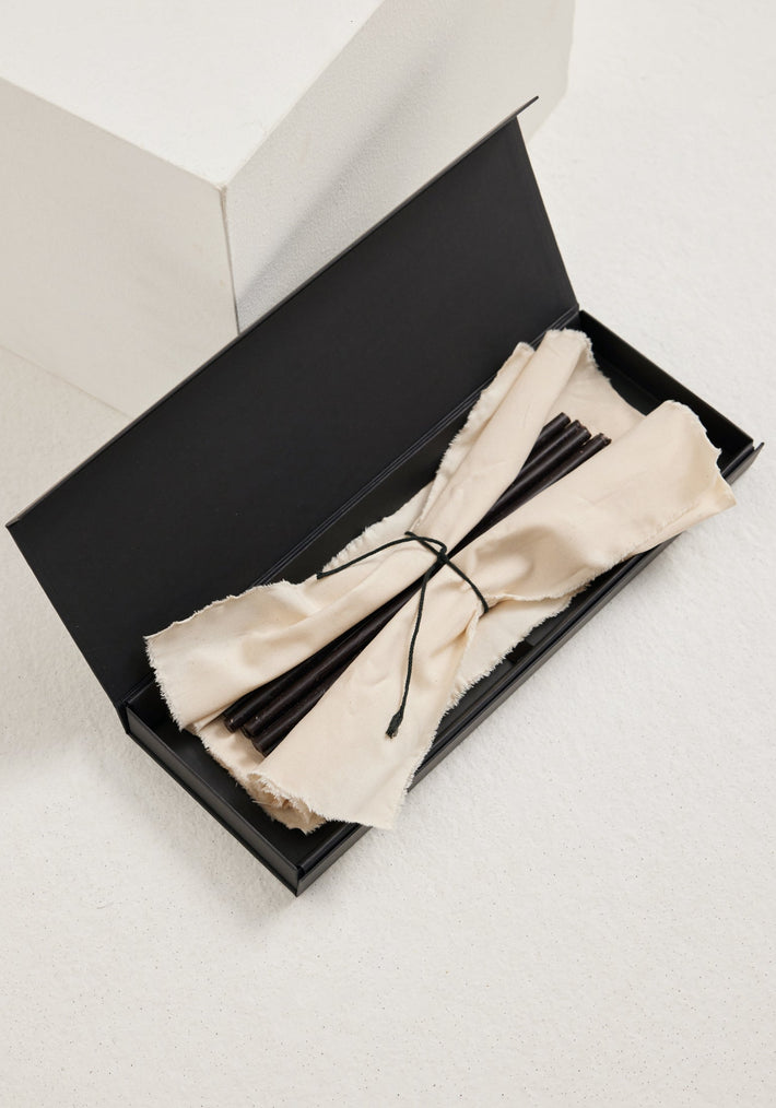 Candles 10mm | noir: A long black gift box with off-white cloth holds slender matte-black beeswax candles, tied with a dark cord, ideal for gifting.