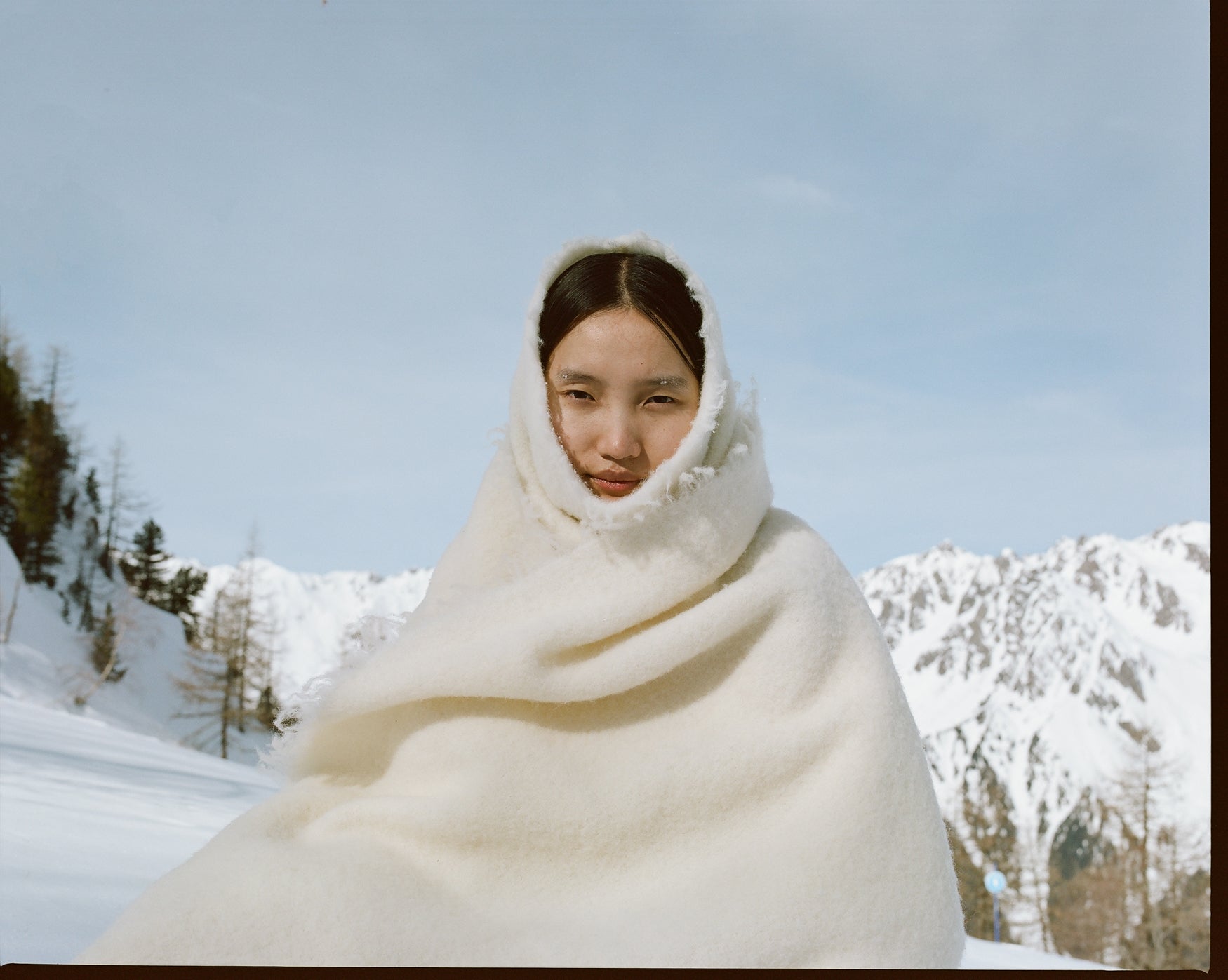 Woman wrapped in a cream wool blanket with snowy mountains in the background and a blue sky