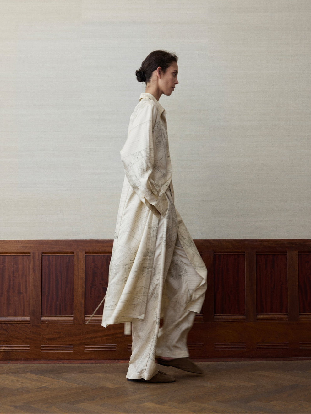 Woman wearing a long silk shirt with a map of Amsterdam printed on it and matching pants against a linen and wood paneled background