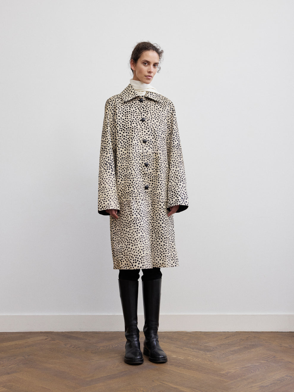 Woman wearing a cheetah print pony hair coat with tall black boots against a white background 