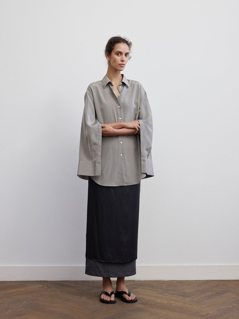 Woman wearing a grey striped satin shirt and navy blue column skirt against a white background