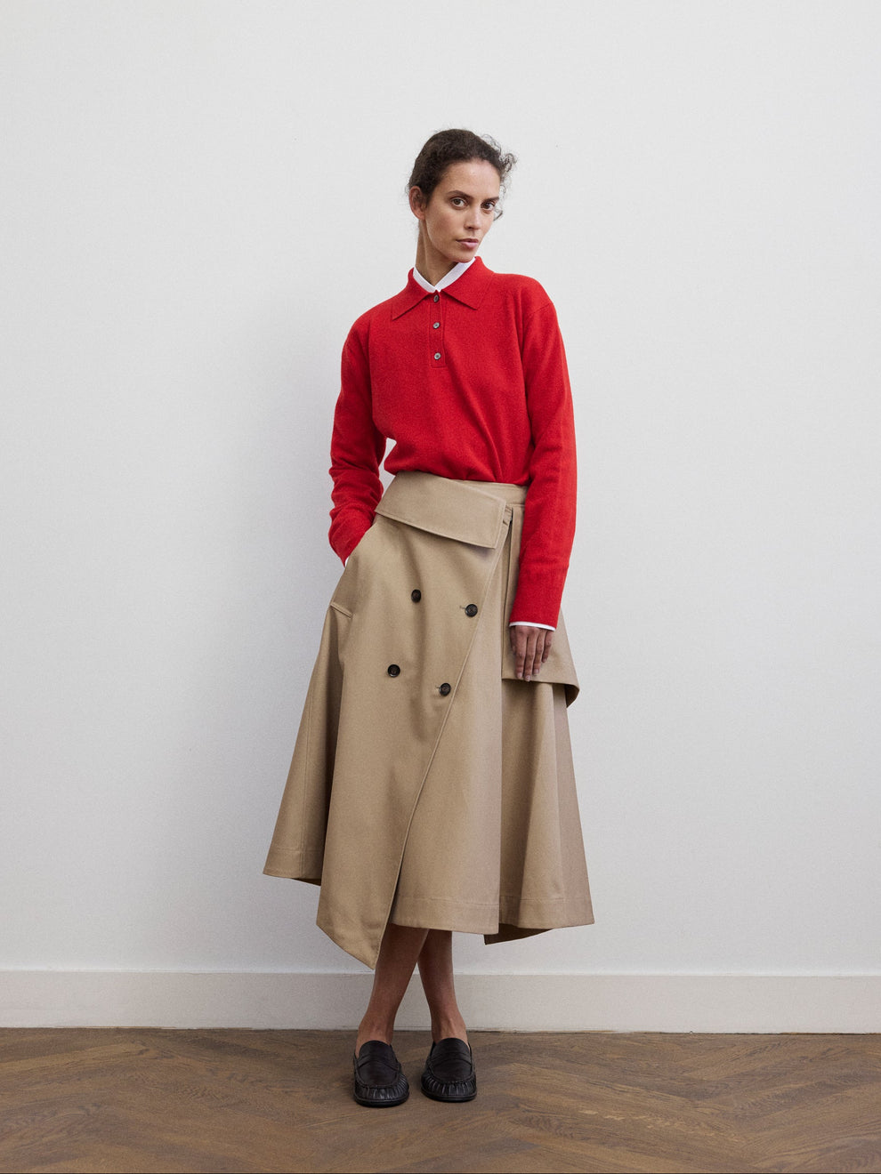 Woman wearing a red wool polo and a skirt inspired by a trenchcoat against a white background 