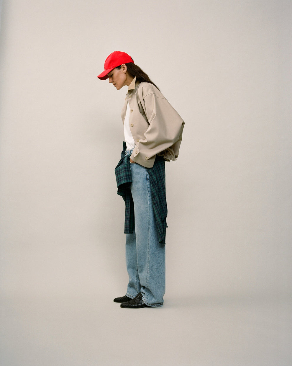 Person wearing a beige short jacket, red cap and jeans against a white backdrop 