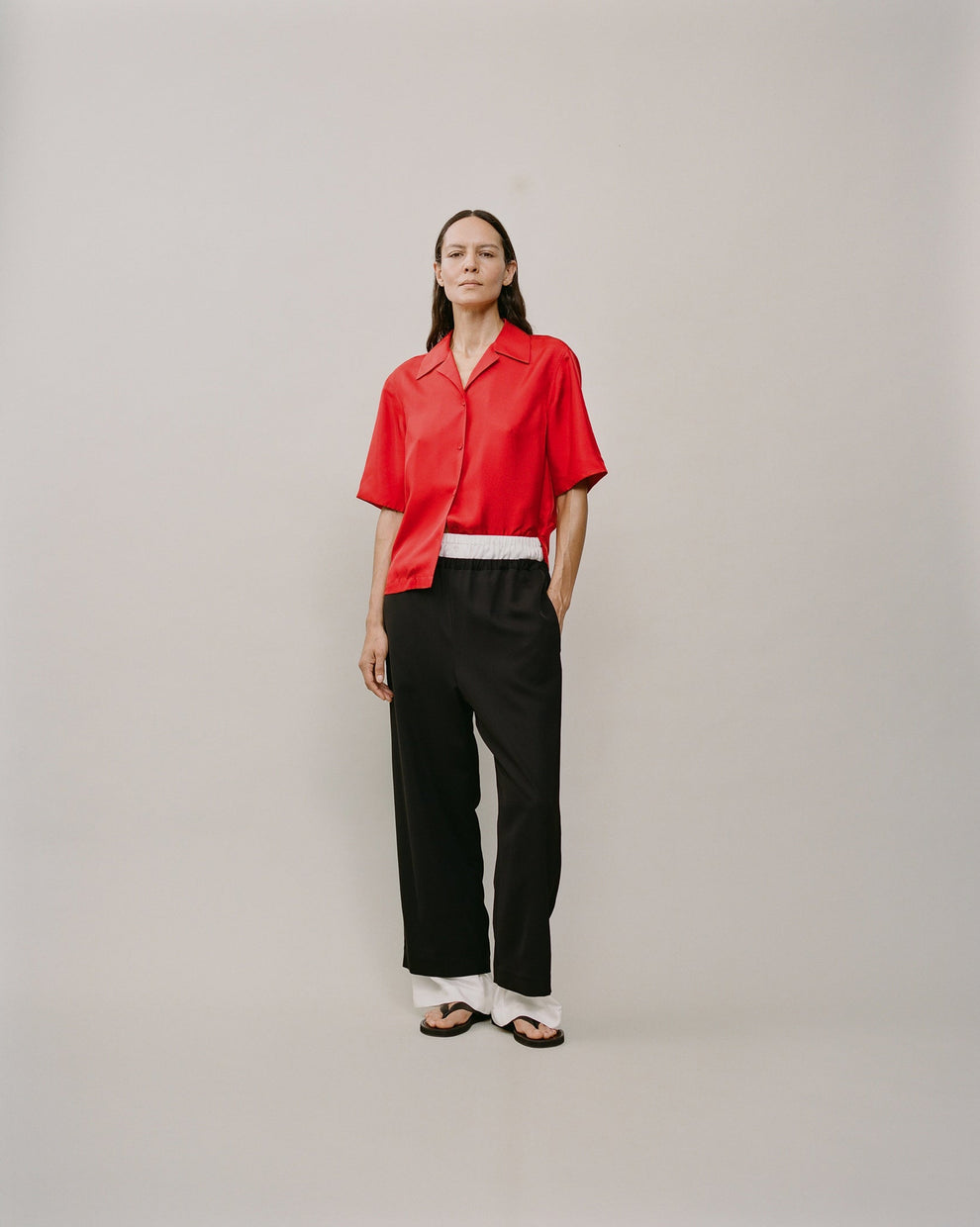 Person wearing a red silk camp collar shirt and black trousers against a white backdrop 