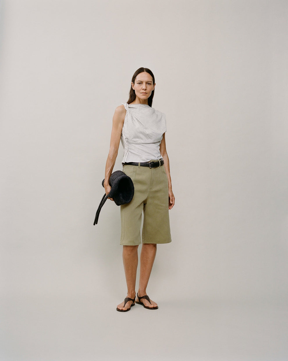 Person wearing a striped top and sage colored shorts against a white backdrop 