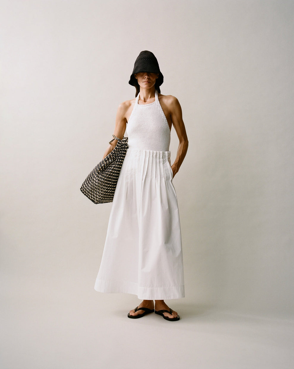 Person wearing a white knitted halter top and white cotton long skirt against a white background 