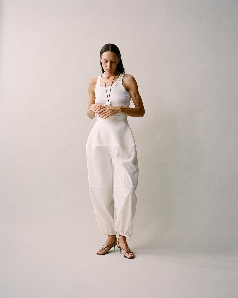 Person wearing a white tanktop and sculptural cream trousers with visible seams 
