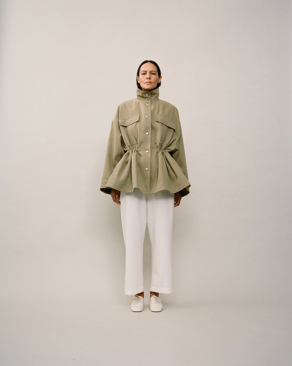 Person wearing a green jacket and white pants on a plain background