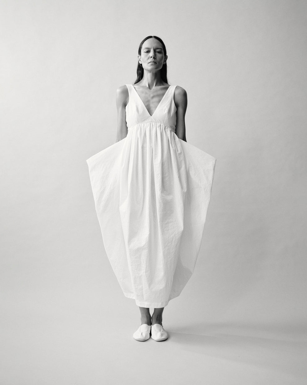 Person wearing a white sculptural dress against a neutral backdrop