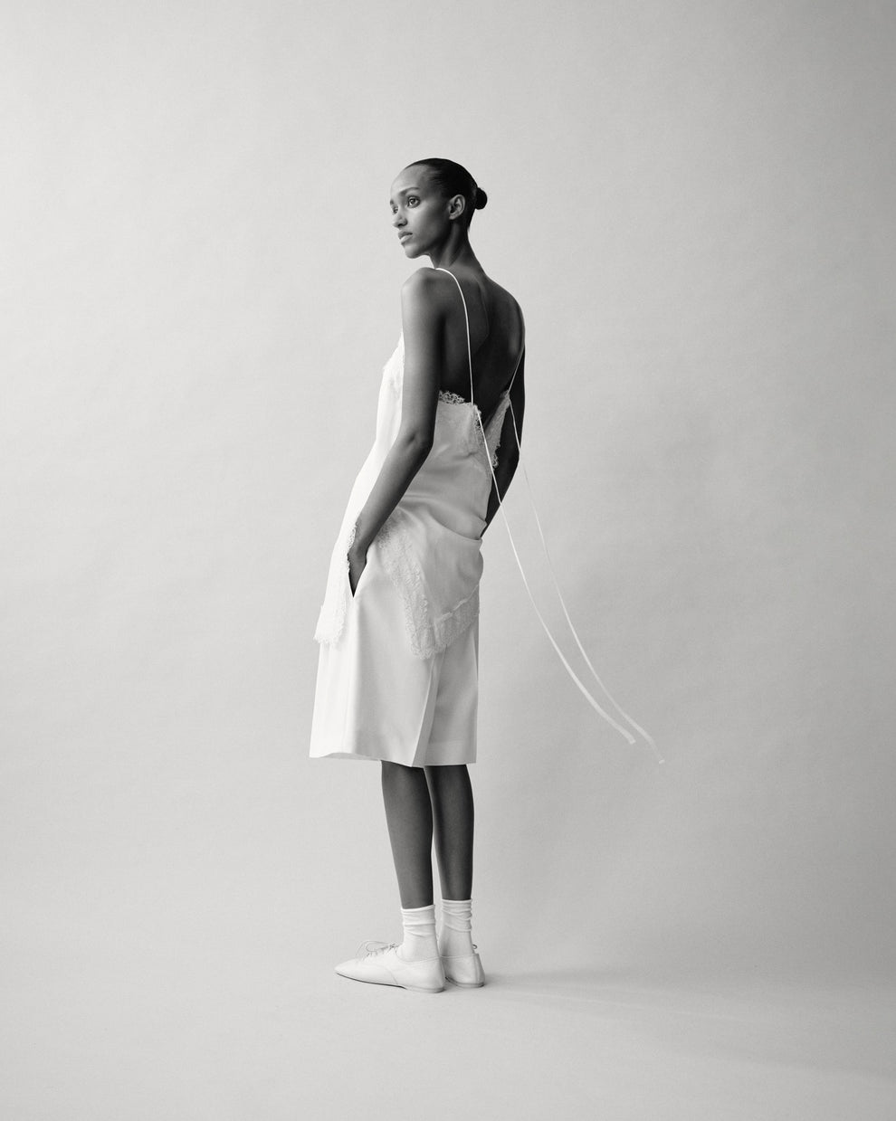 Person wearing a lace camisole top and cream tailored shorts against a white backdrop 