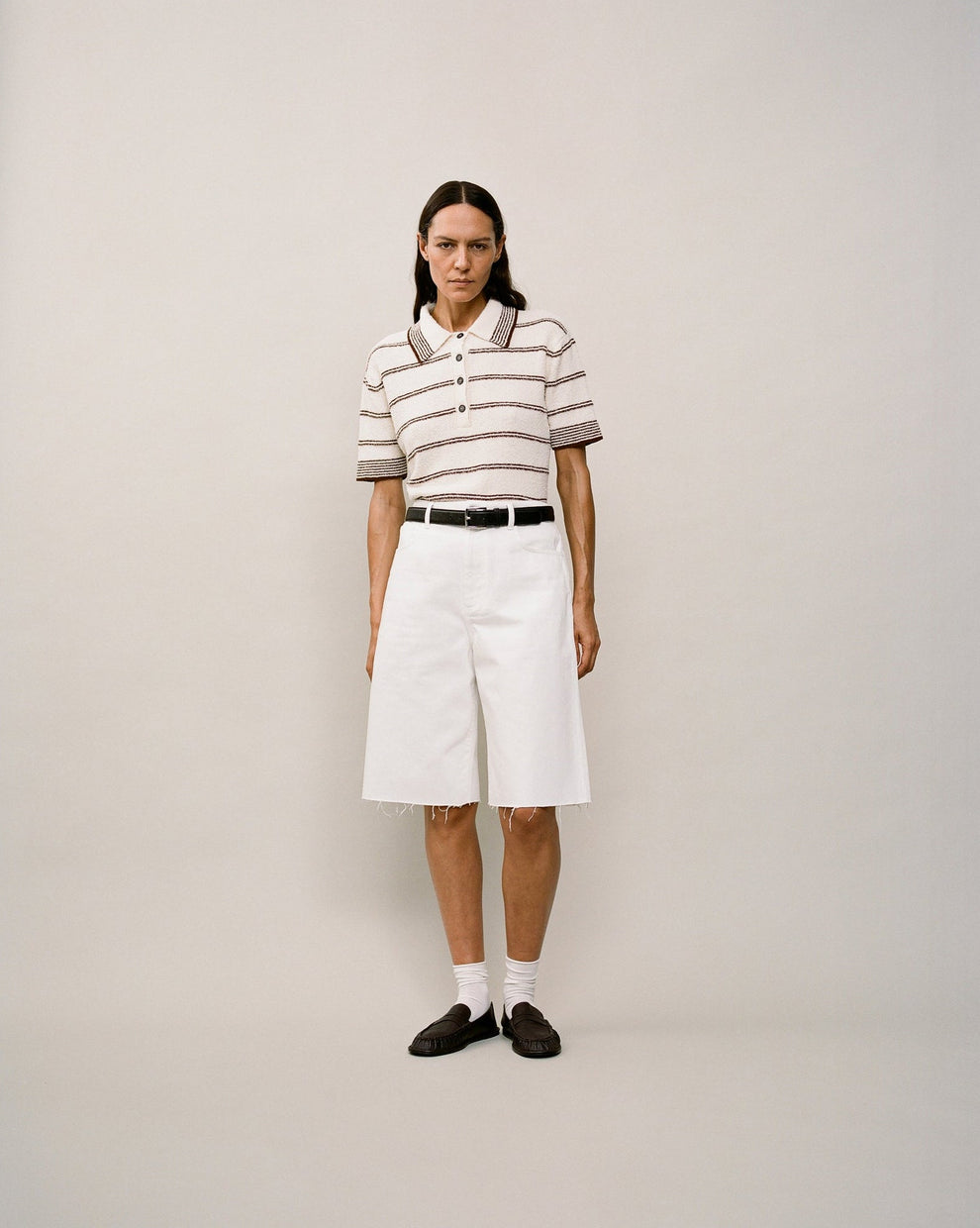 Person wearing a striped short sleeve polo and white shorts against a white backdrop