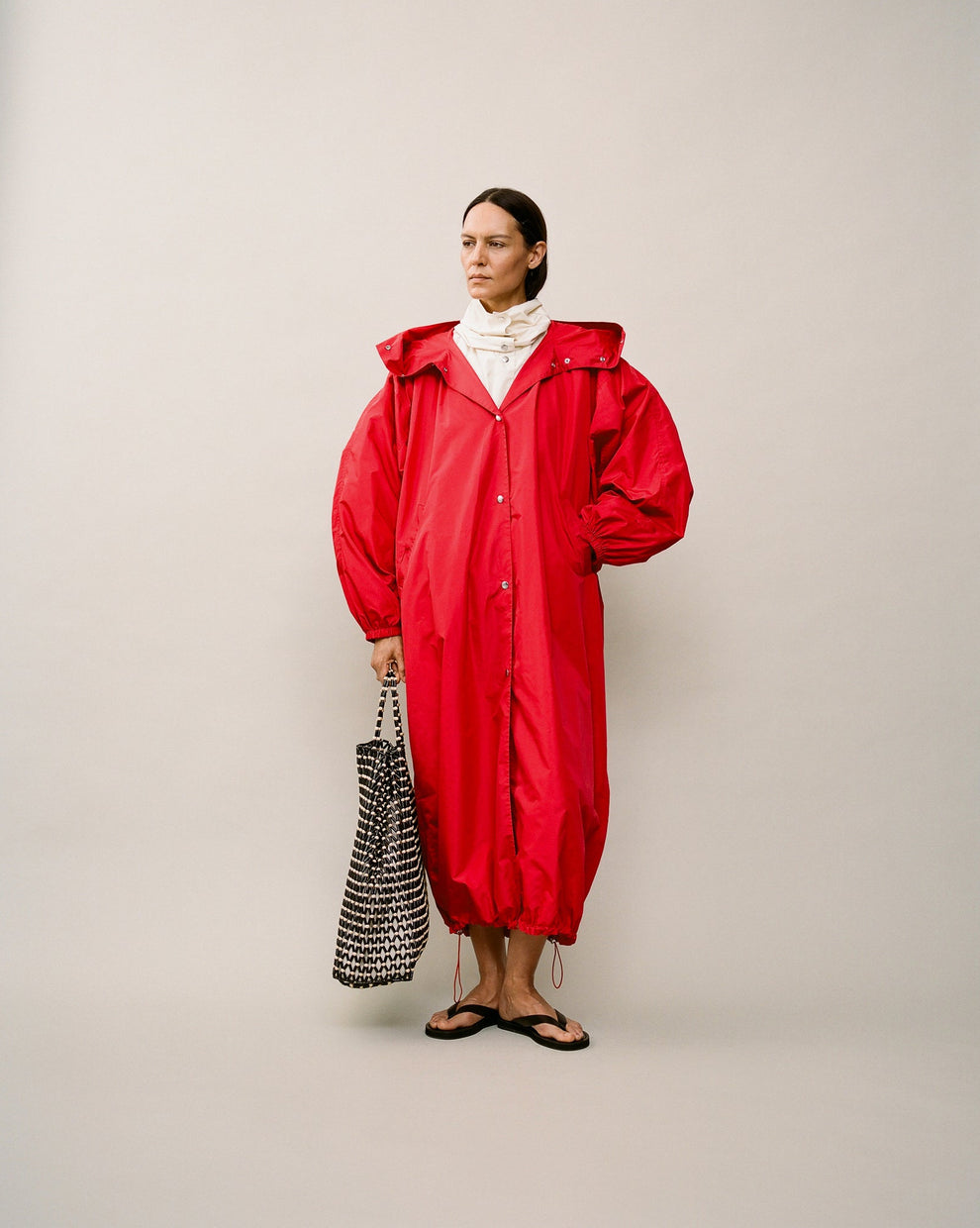 Person wearing a long red parka coat against a white backdrop