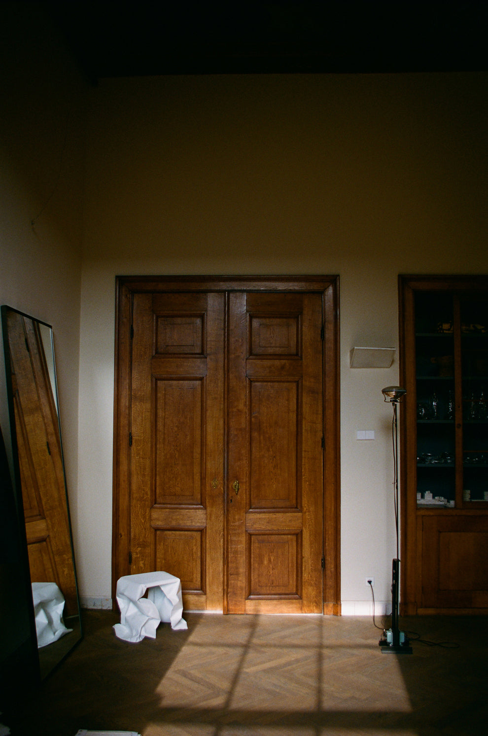 Wooden door in a room with a light source casting shadows on the floor and a white paper looking stool in front
