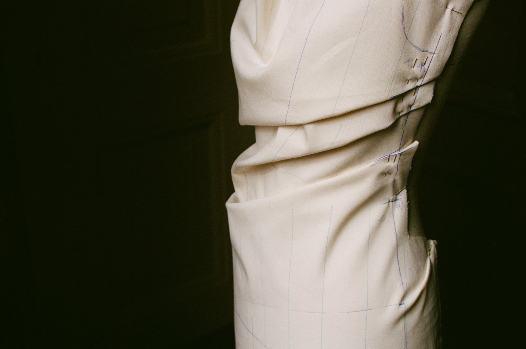 Close-up of canvas fabric draped on a mannequin with pins and sketch lines with a dark background