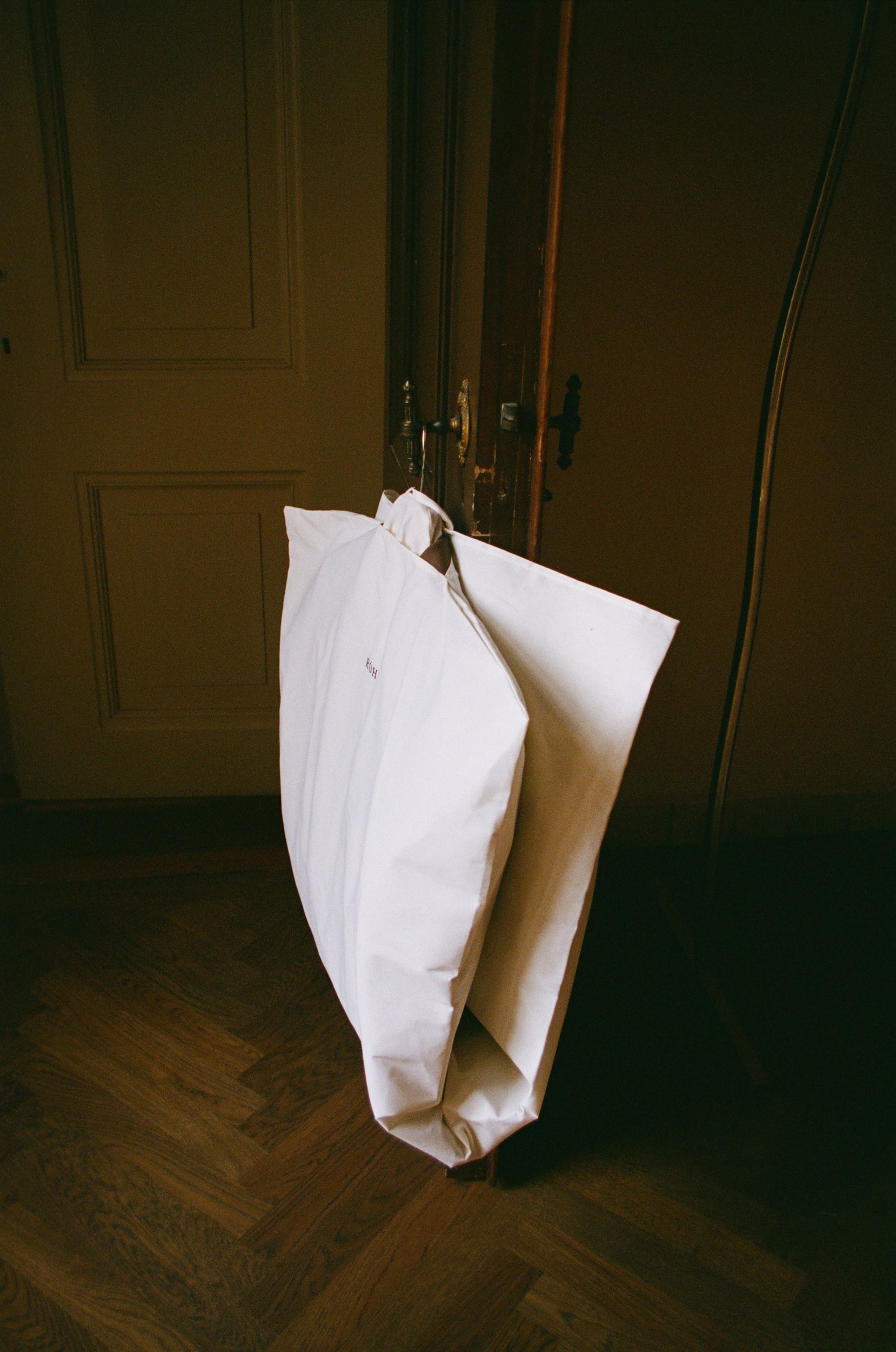 Garment bag hanging from a door handle in a dimly lit room with wooden flooring.
