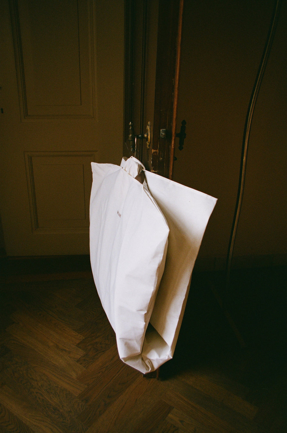 Garment bag hanging from a door handle in a dimly lit room with wooden flooring.