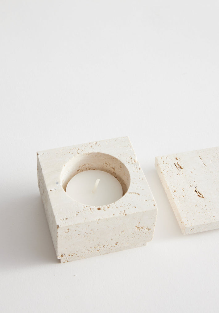 Tealight box | travertine: A handcrafted square travertine box with a circular recess holding a white tealight, accompanied by a matching flat lid.