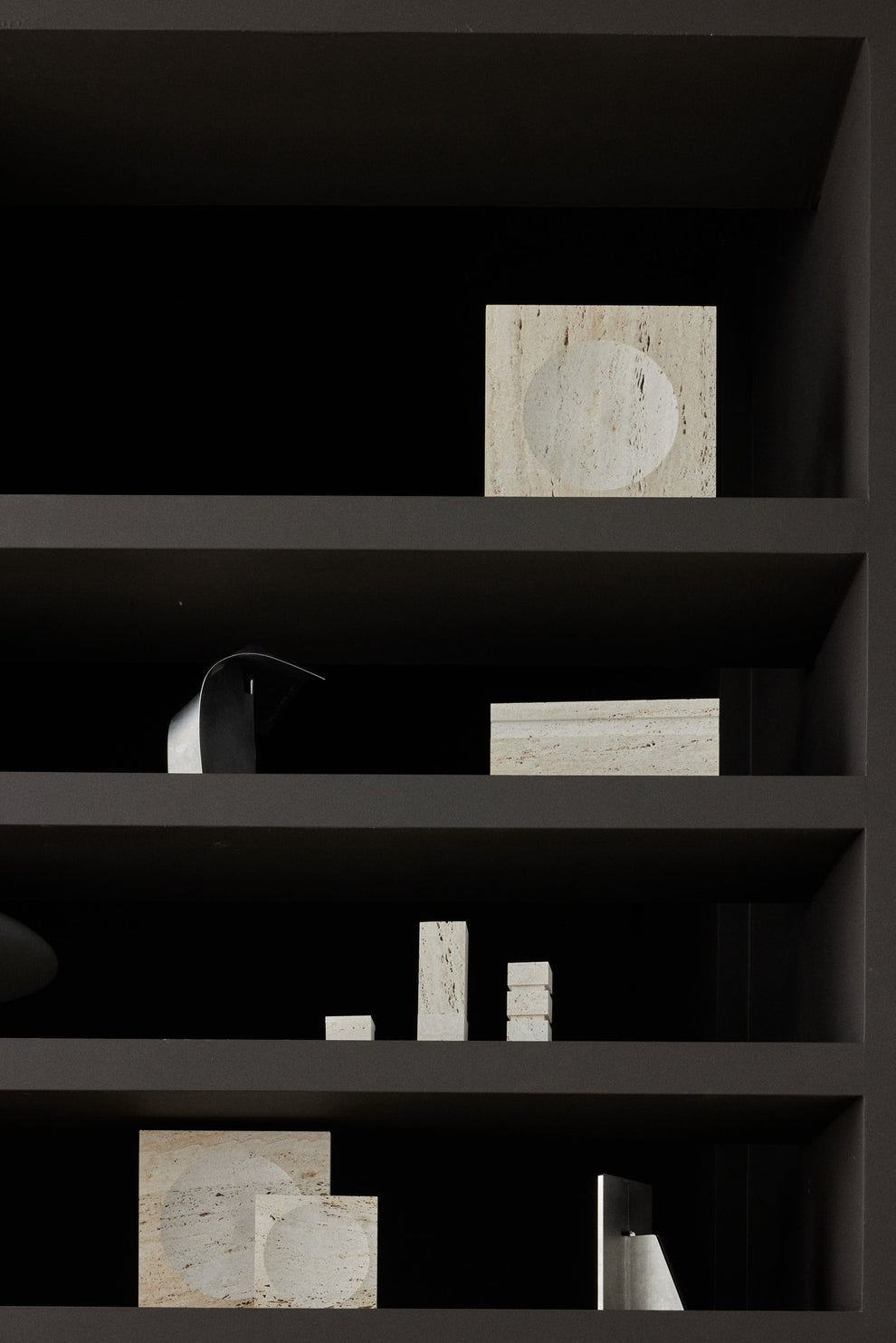 Dark shelving unit with various cylindrical travertin objects and a square item on a black background