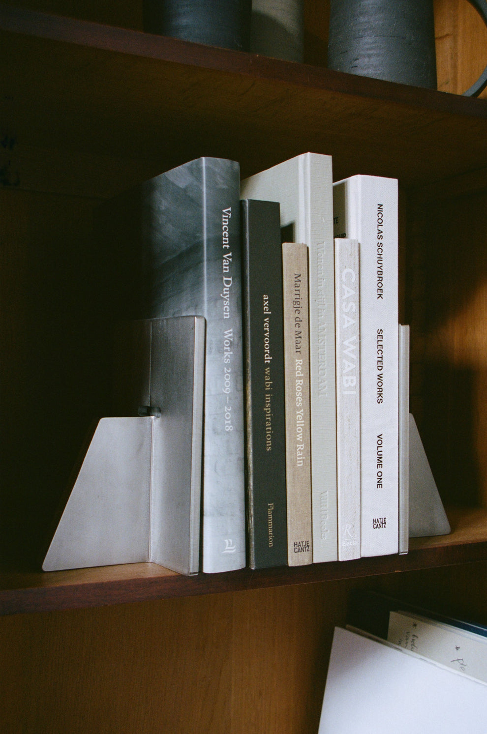 Books on a wooden shelf with stainless steel heavy brutalist book ends