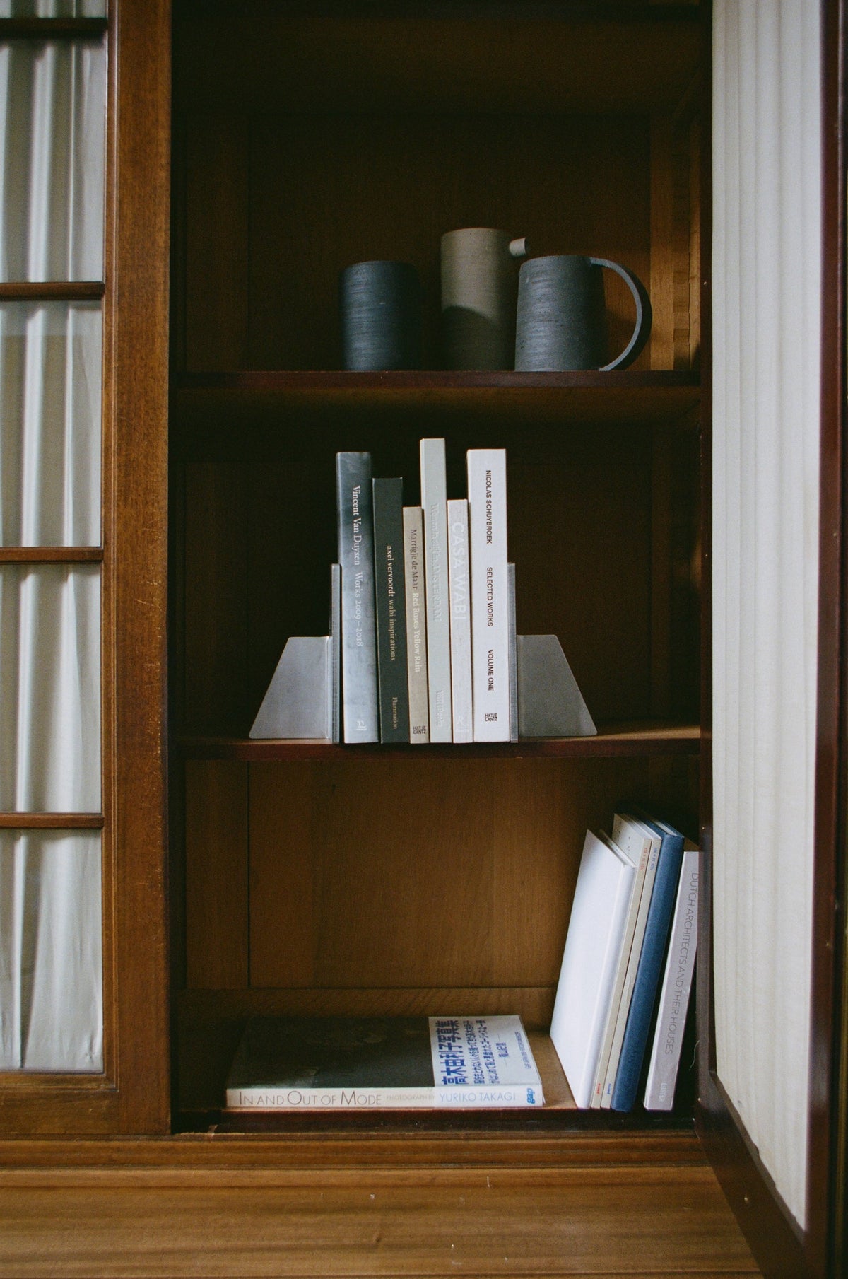 Stainless steel bookends securely support hardcover books on a wooden shelf, showcasing minimalist triangular design by Dutch designer Paul Coenen, crafted with 8mm thick stainless steel.