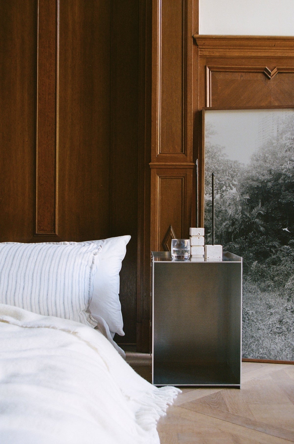 Two-way cube candleholder in travertine sits on a metal bedside table, showcasing its versatile design amidst a minimalist bedroom setting.