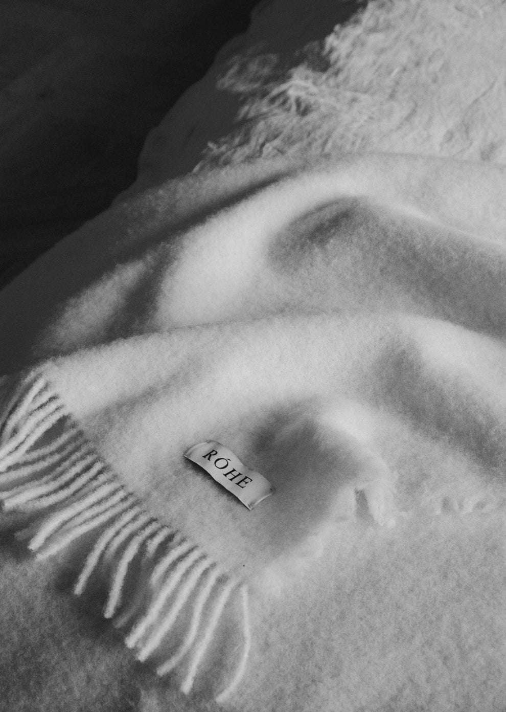Black and white image of a textured wool blanket with fringes with 'Róhe' label in the corner