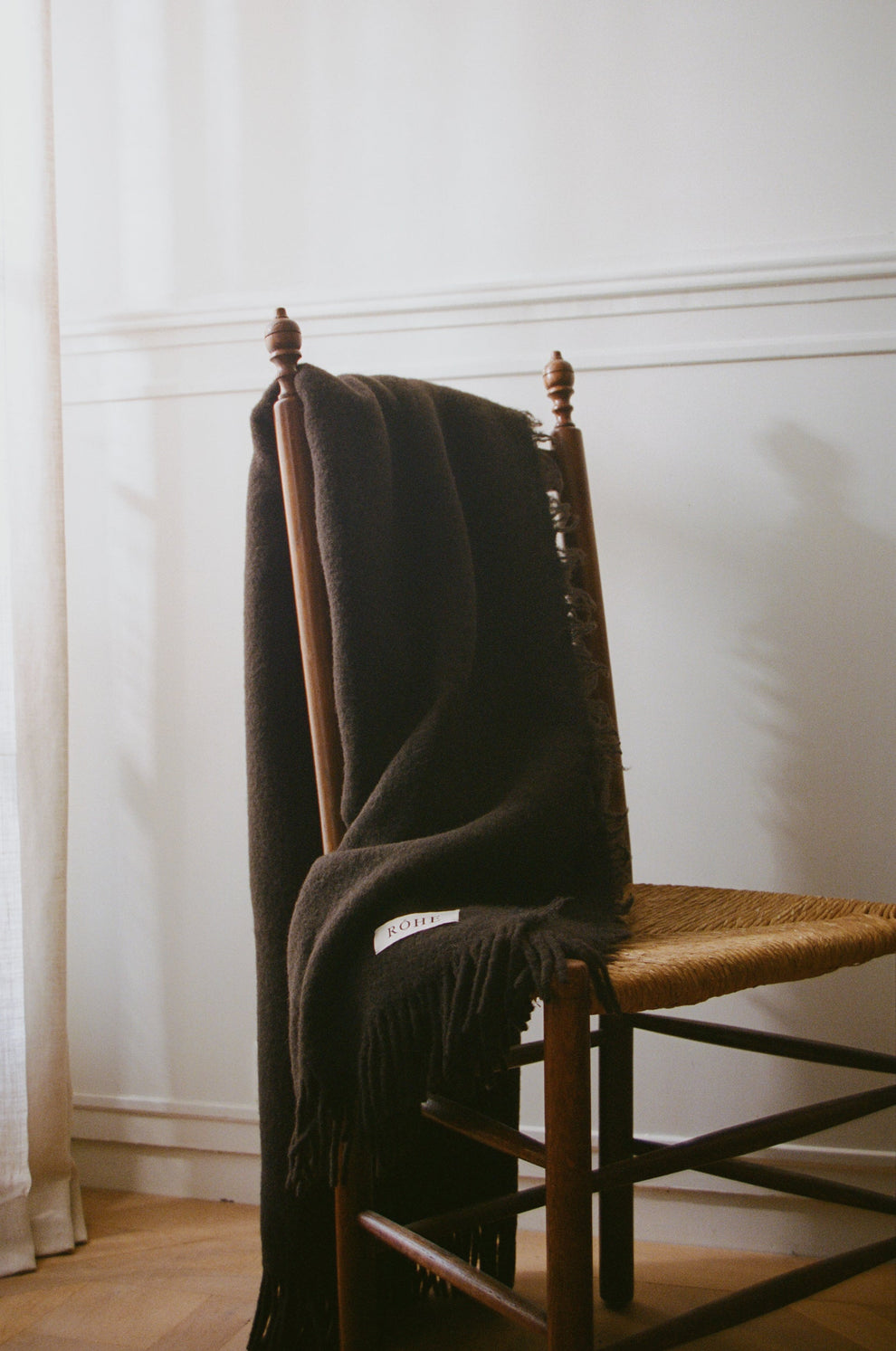Brown blanket draped over a wooden chair against a white wall.
