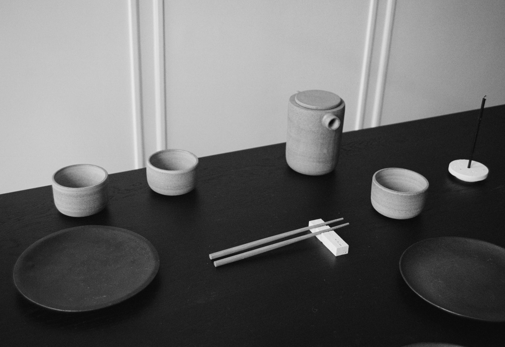 Set of ceramic dishes and a teapot on a black surface with a white background