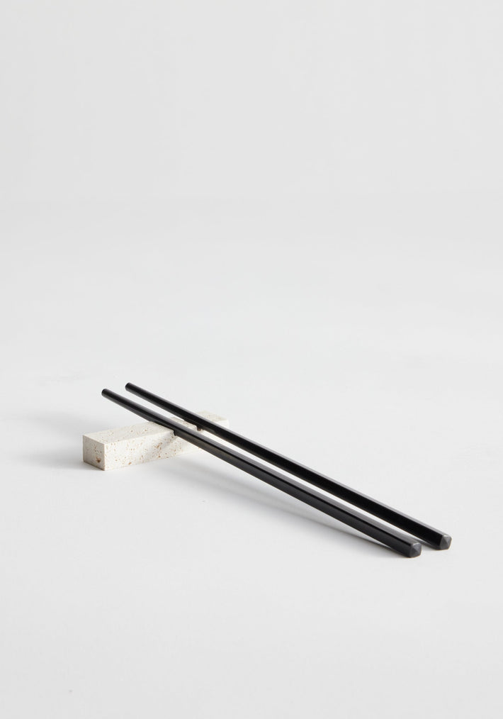Chopstick holders | travertine, featuring a black chopstick on a handcrafted stone rest made from Italian travertine, showcasing artisanal Dutch craftsmanship by Louis Crombag.
