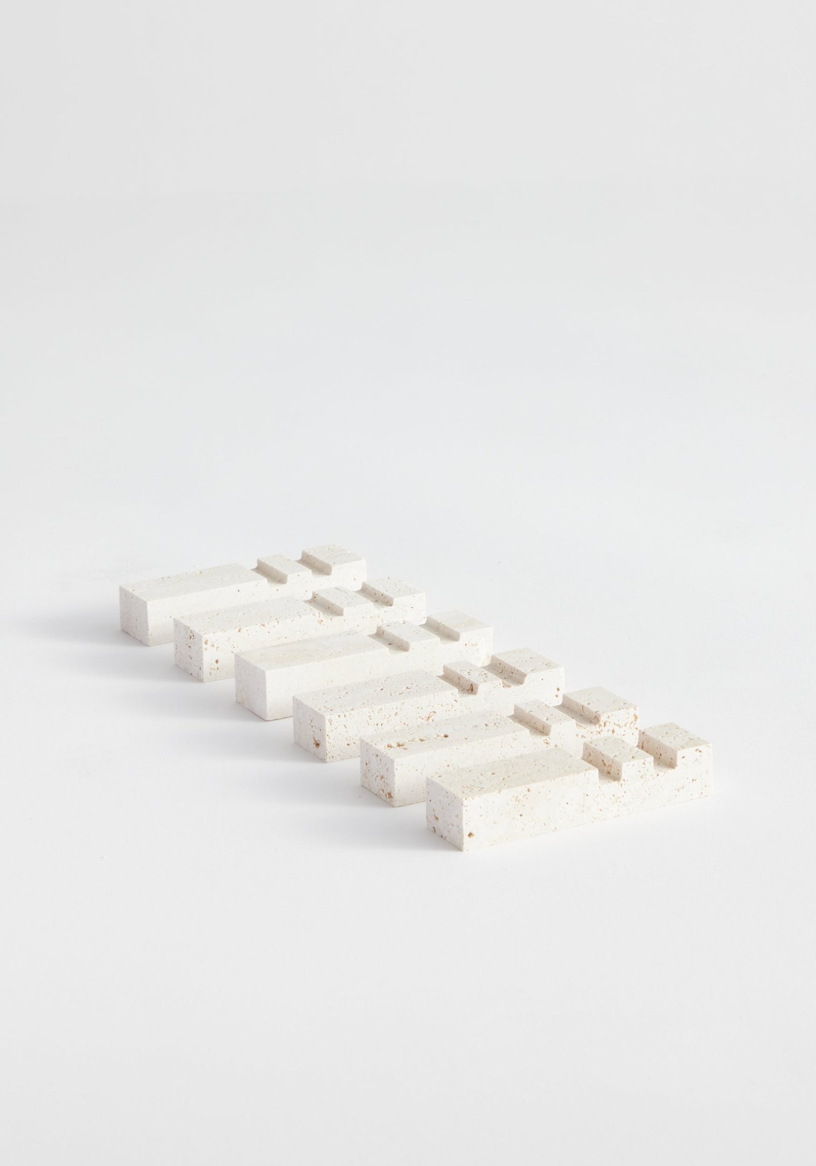 Chopstick holders | travertine: A series of speckled rectangular travertine blocks in stepped arrangements, handcrafted by Louis Crombag from Italian travertine, showcasing unique textures.