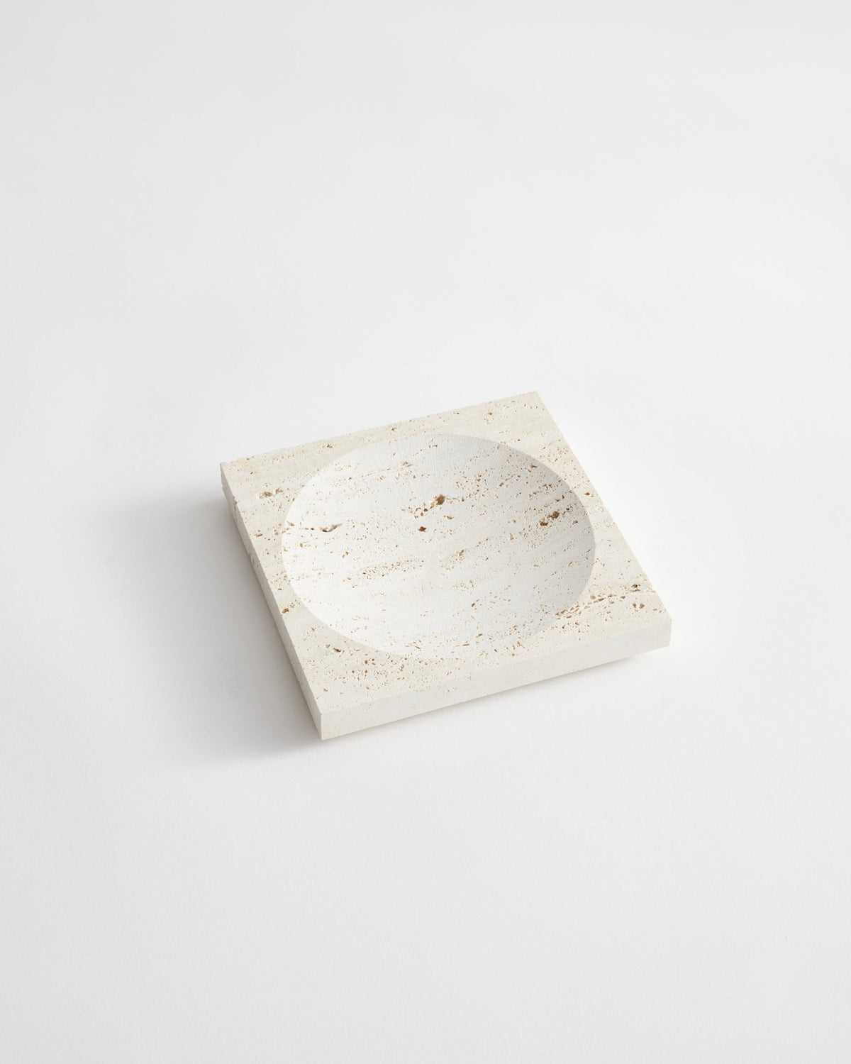 Small tray | travertine: A handcrafted, pale-beige square stone tray with a round carved indent, made from Italian travertine by Dutch artist Louis Crombag.
