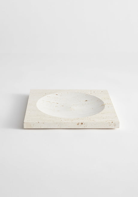 Medium tray | travertine: A square travertine block with a round, shallow indent, handcrafted by Louis Crombag, showcasing its natural porous texture and unique design.