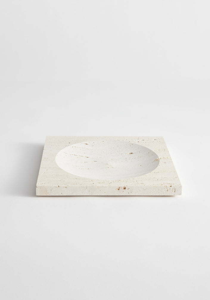 Medium tray | travertine: A square travertine block with a round, shallow indent, handcrafted by Louis Crombag, showcasing its natural porous texture and unique design.