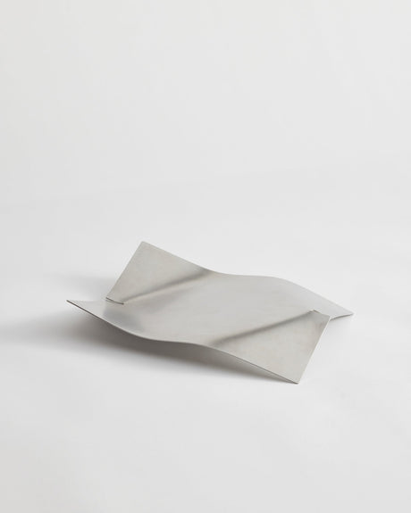 Stainless steel bowl in a wave shape, handcrafted from a single sheet, showcasing a minimalist design by Dutch designer Paul Coenen, on a white background.