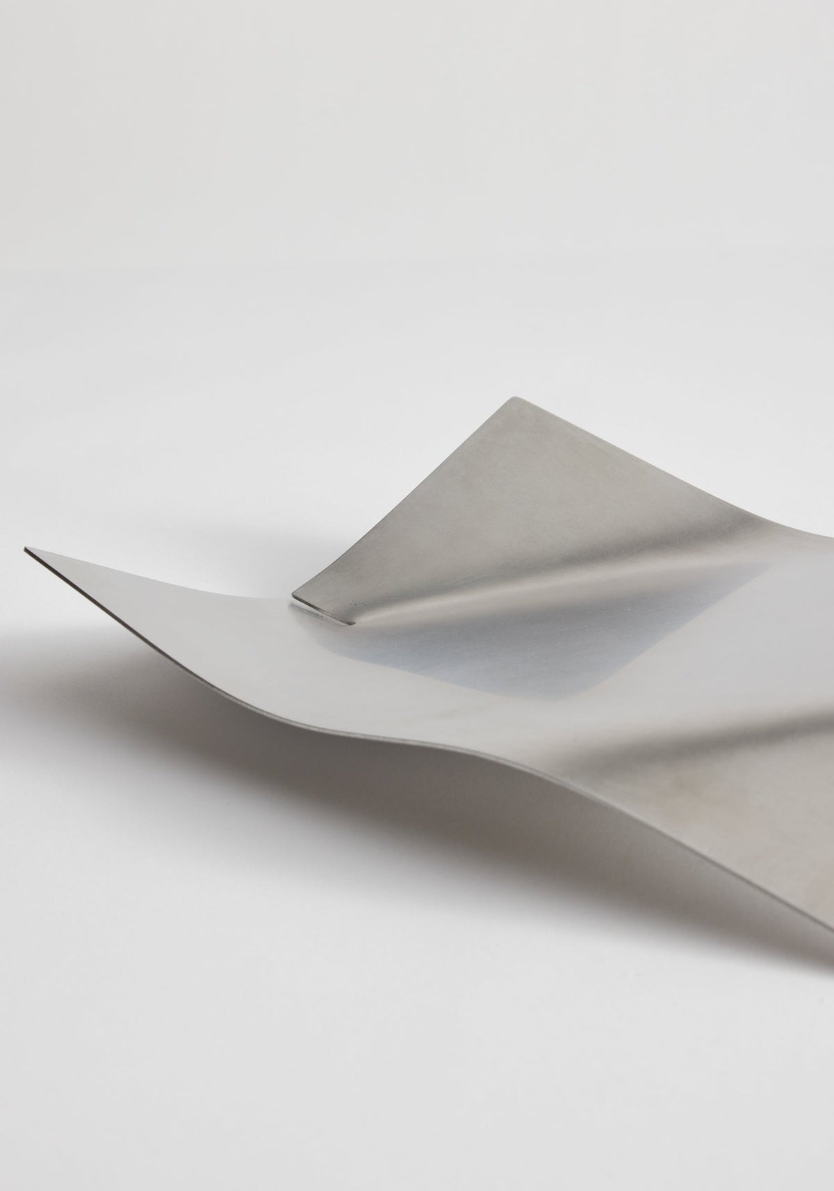 Stainless steel bowl in a minimal bended shape, featuring overlapping, wave-like curves, handcrafted in the Netherlands from thin stainless-steel sheets.
