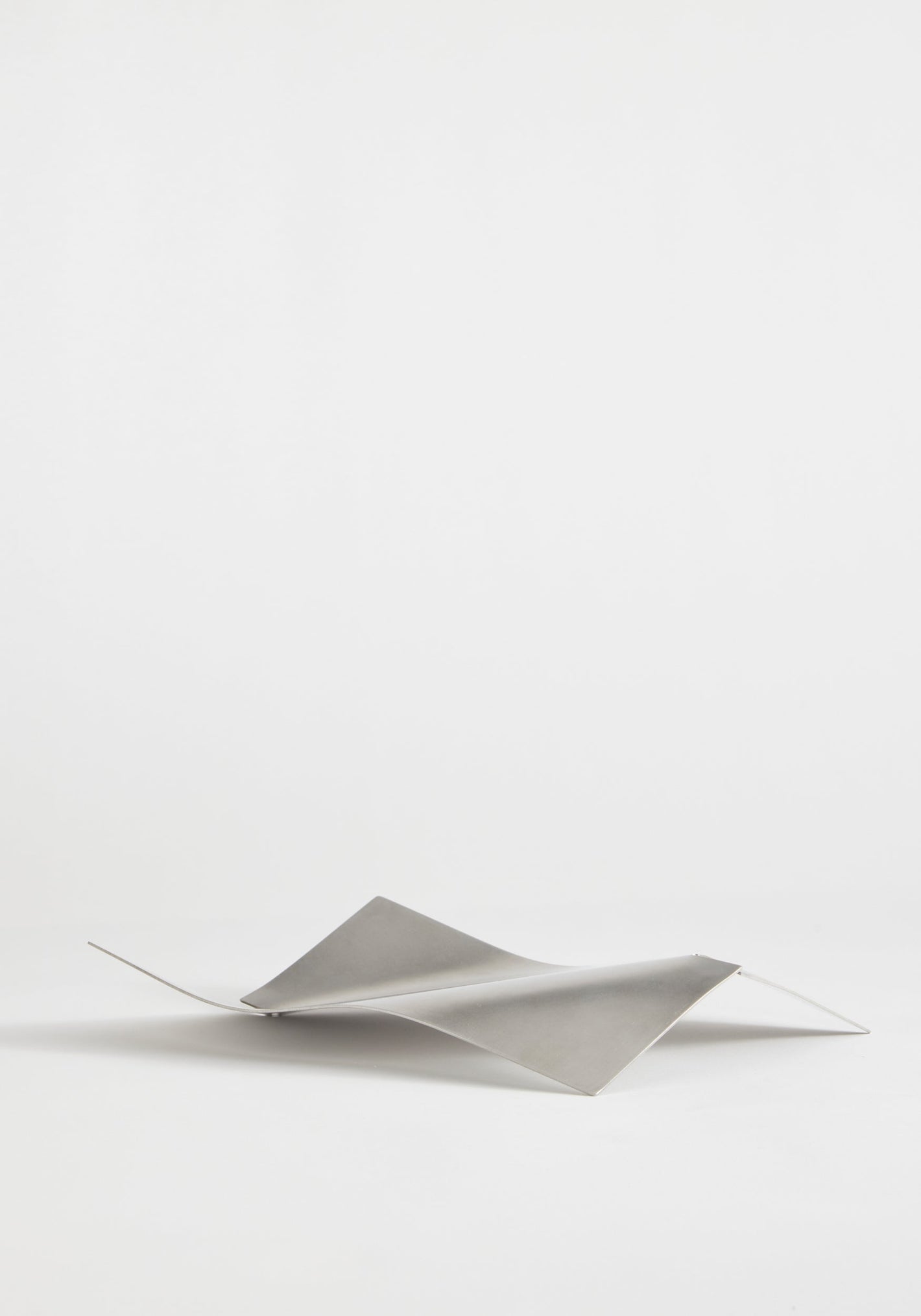 Stainless steel bowl in a wave shape, handcrafted from a single sheet, showcasing a minimalist design by Dutch designer Paul Coenen, on a white background.