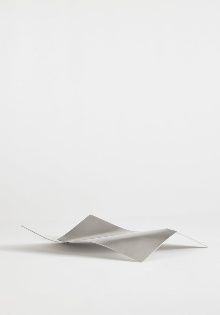 Stainless steel bowl in a wave shape, handcrafted from a single sheet, showcasing a minimalist design by Dutch designer Paul Coenen, on a white background.