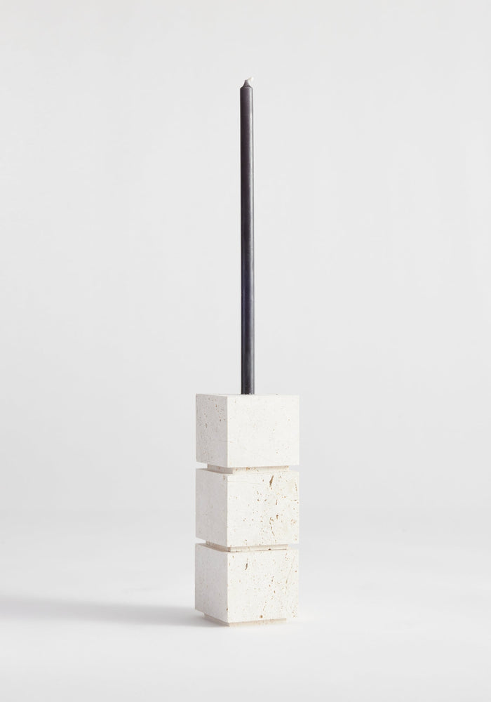 Sculptural candle holder small | travertine: Three stacked stone cubes with a black taper candle, handcrafted from Italian travertine by Dutch artist Louis Crombag.