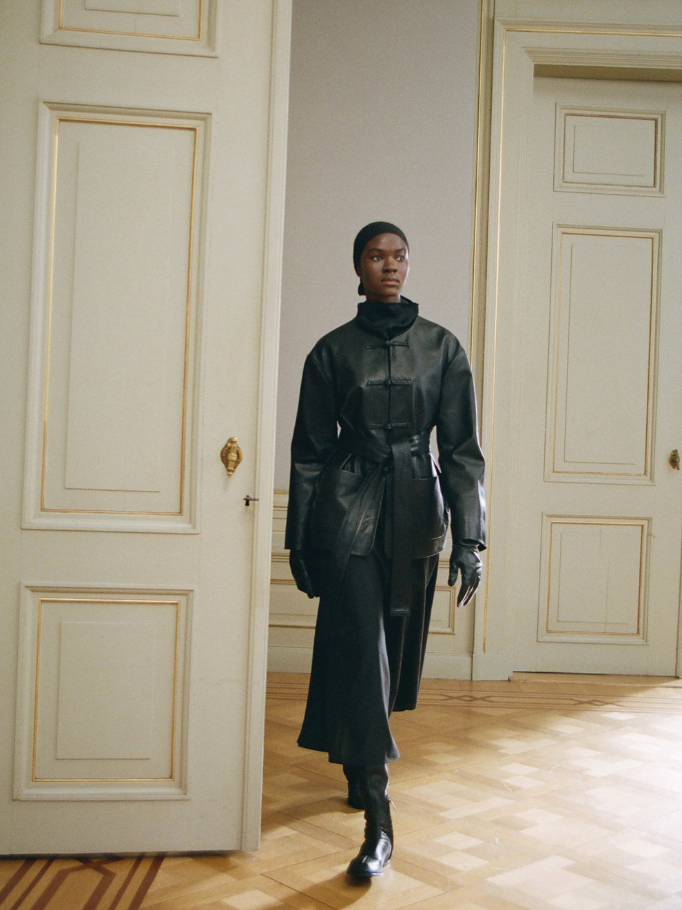 Person wearing a black leather jacket and black skirt in an elegant room with wooden floor and paneled walls