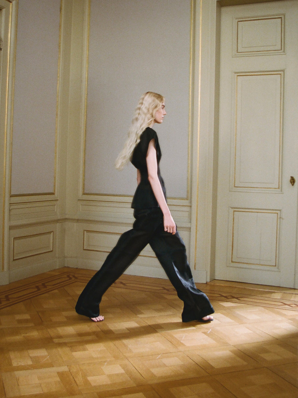 Woman walking in a room in a black outfit with wooden flooring and paneled walls