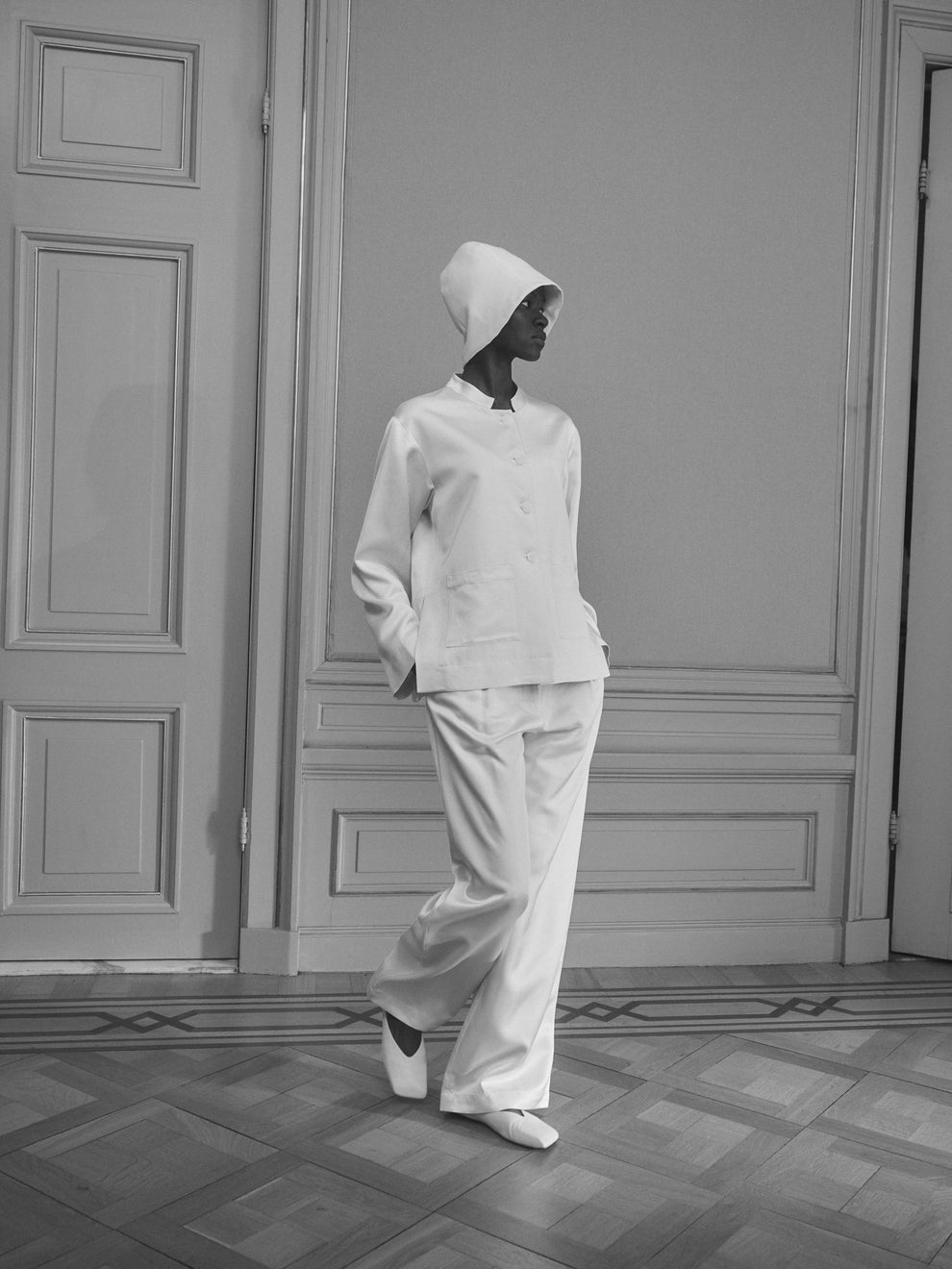 Woman wearing a white satin outfit with a hat in an elegant room with paneling.