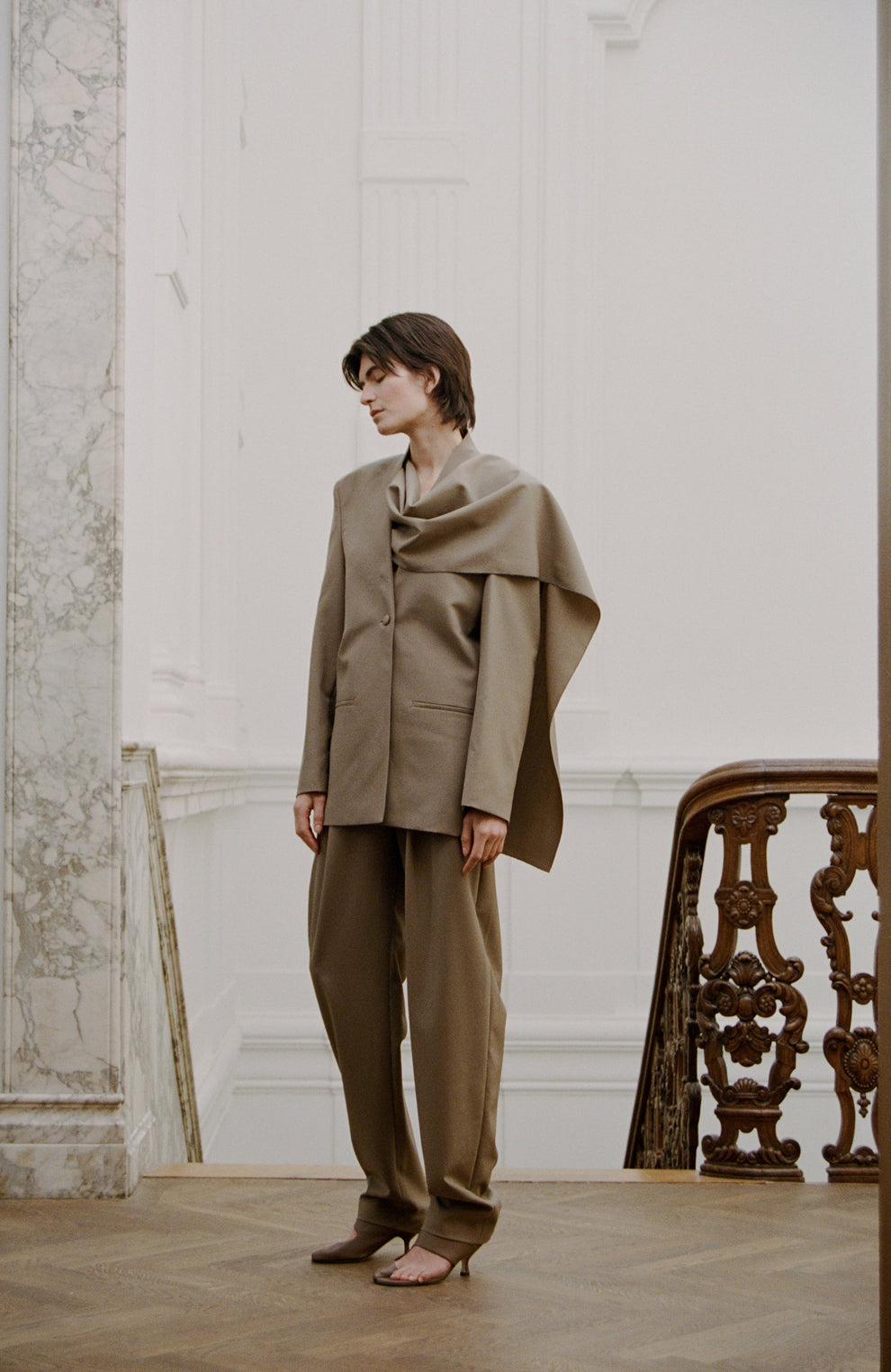 Woman wearing a sage colored suit standing in an elegant room with wooden furniture.