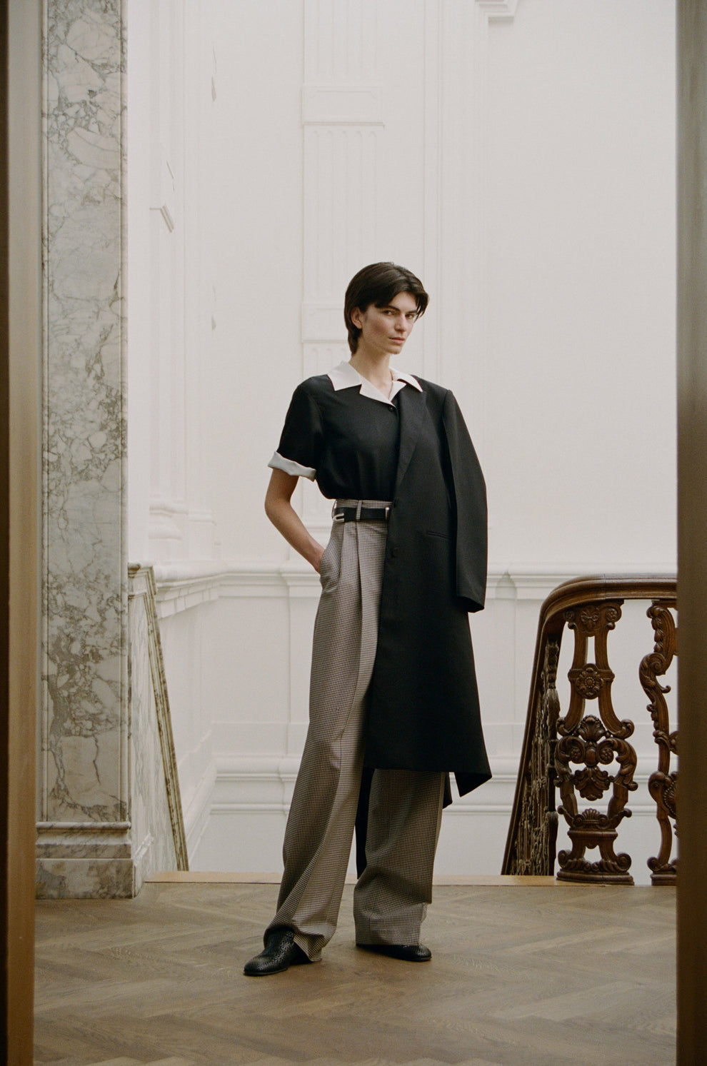 Woman wearing a black and white camp collar shirt and gingham print trousers standing in an elegant interior