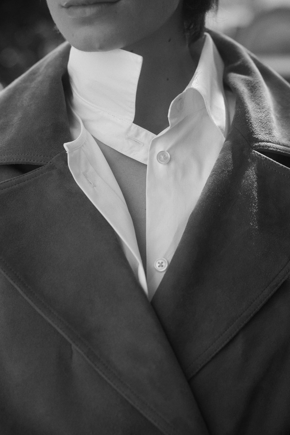 Close-up of a person wearing suede coat over a white deconstructed shirt with a blurred background