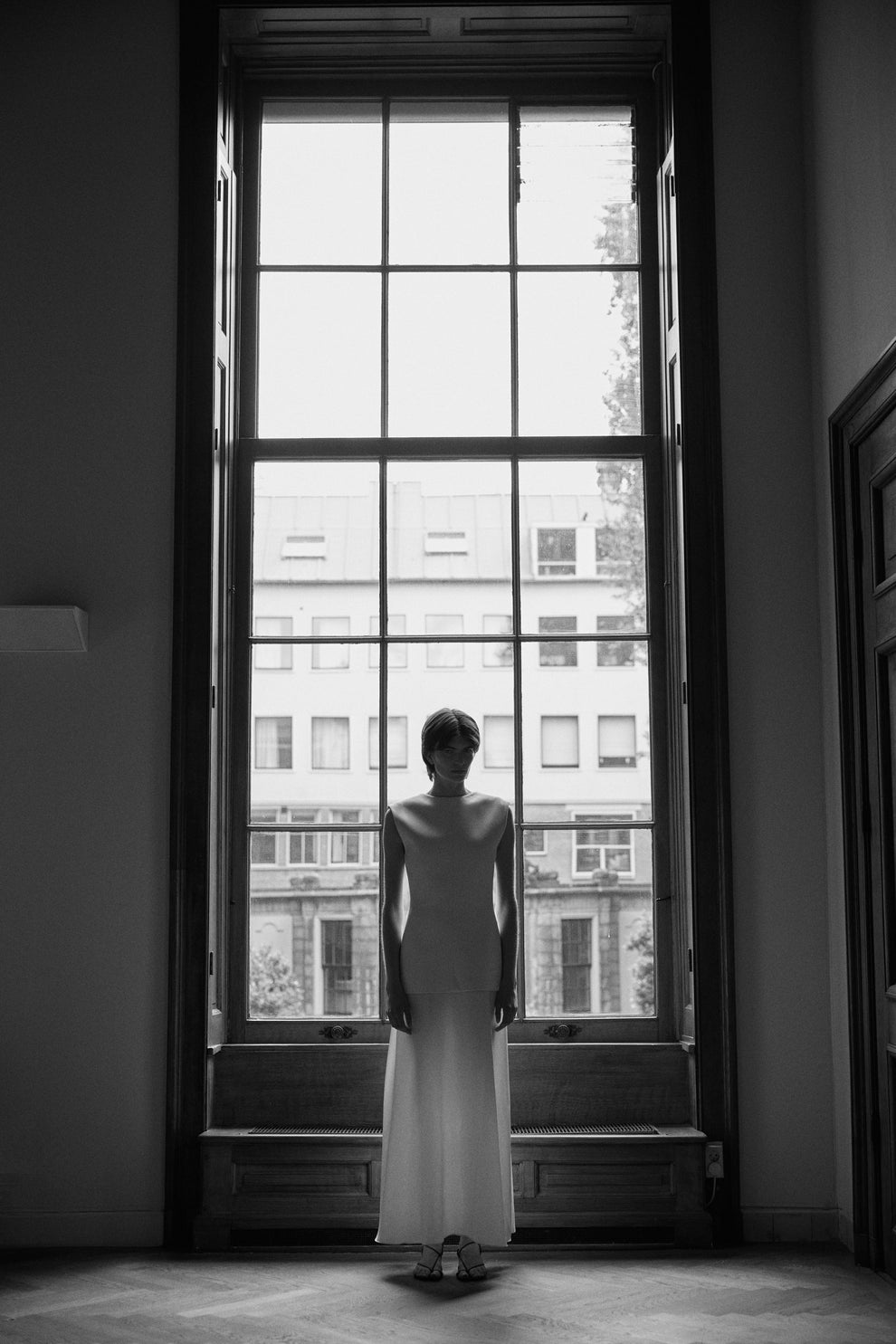 Woman in a white dress standing in front of a large window with cityscape view