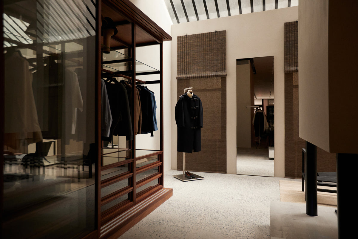Modern clothing boutique interior with dark wood and glass wardrobes holding garments a mannequin in black clothing mirrors and striped ceiling shadows